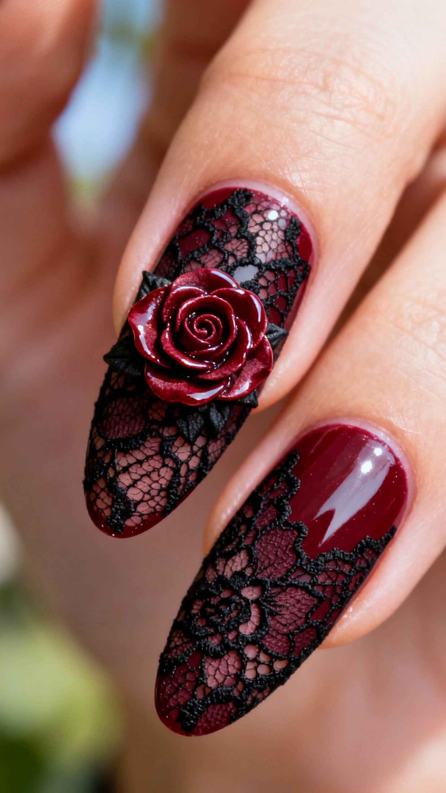 Closeup almond nails, burgundy base with black lace, single glossy rose detail