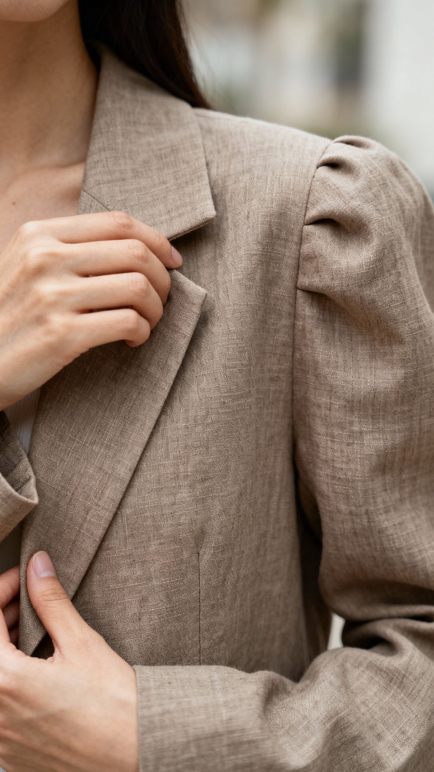 Closeup of female hands adjusting taupe boxy blazer lapel, padded shoulders, linen texture