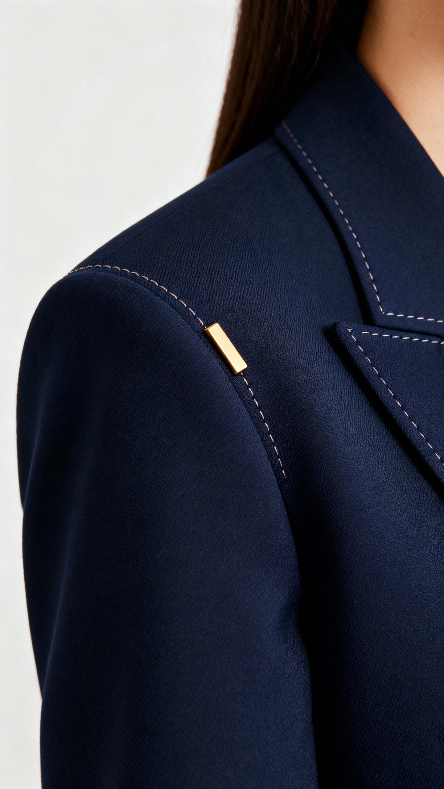 Closeup of navy blazer shoulder seam and stitching, brushed gold minimal hardware