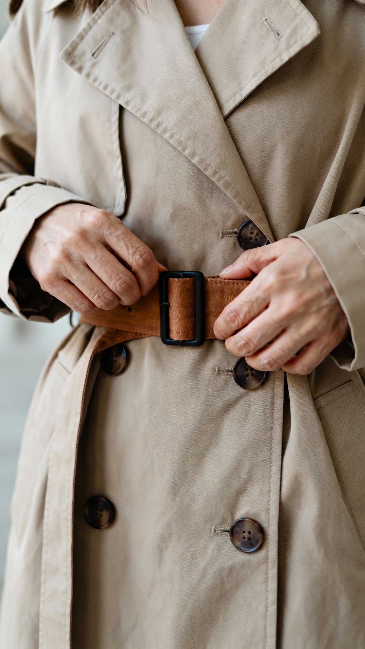 Closeup of petite woman adjusting trench belt higher