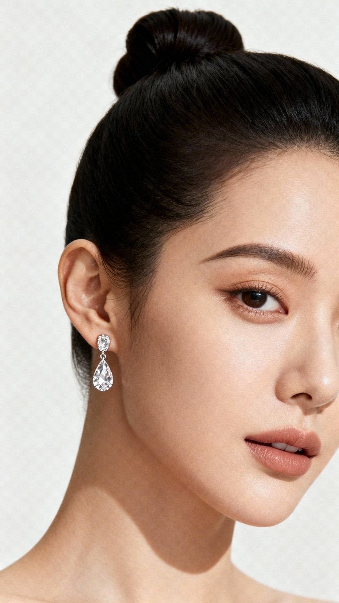 Crystal drop earrings beside sleek bun, minimal makeup closeup