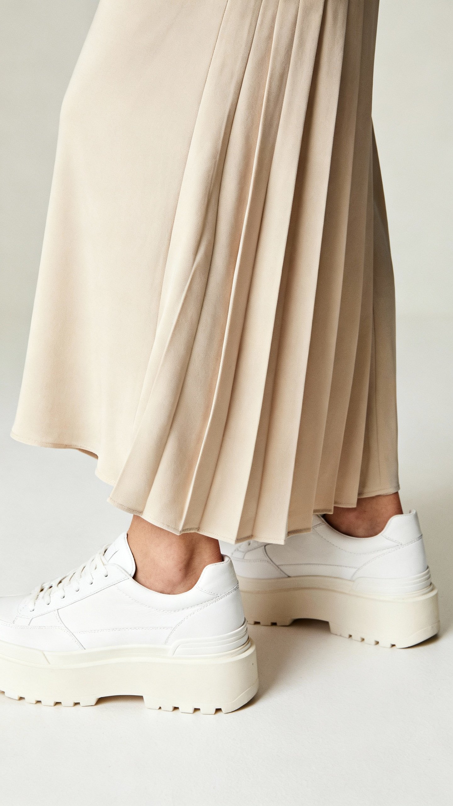 Detail shot midi skirt hitting slim lower calf, bias-cut drape, platform sneakers, ankle showing