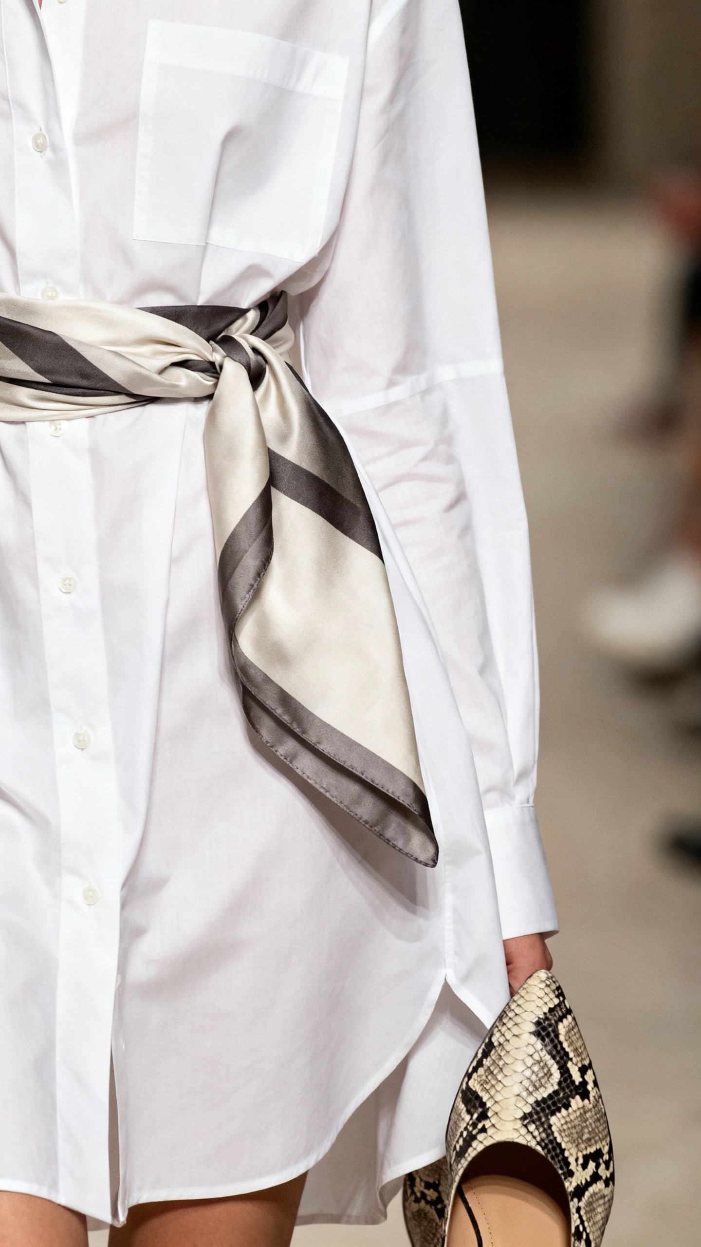 Closeup of white poplin shirt with silk scarf belt, snakeskin shoes peeking
