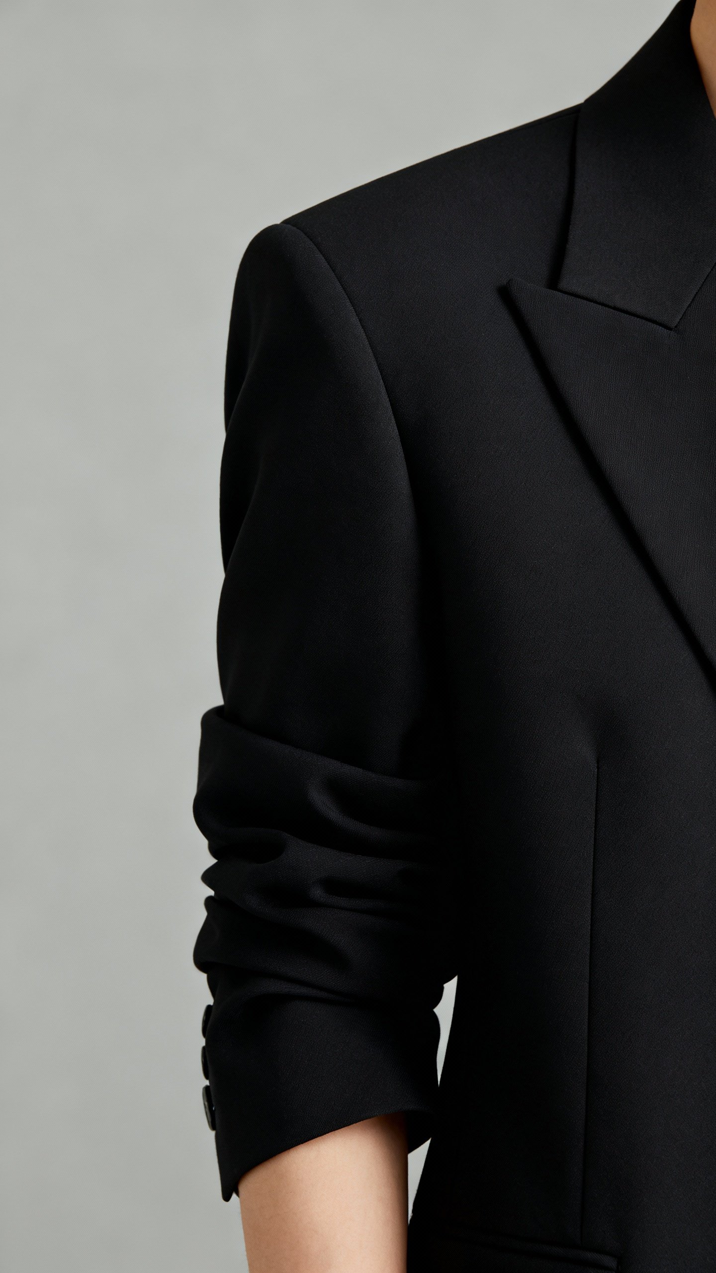 Detail shot of structured black blazer shoulder seams aligned, sleeve pushed to wrist bone