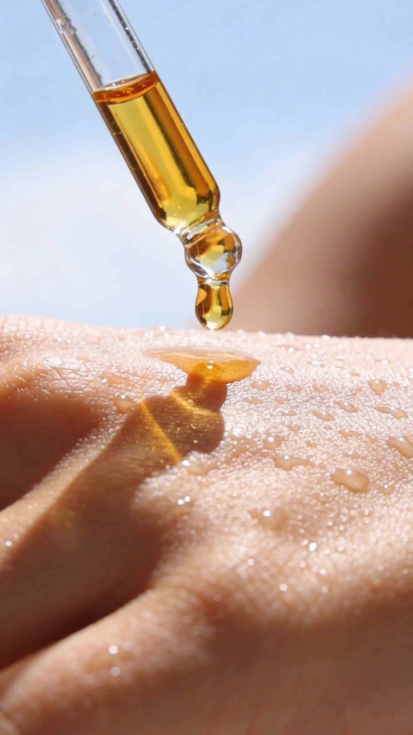 Face oil dropper over dewy summer skin, bright daylight