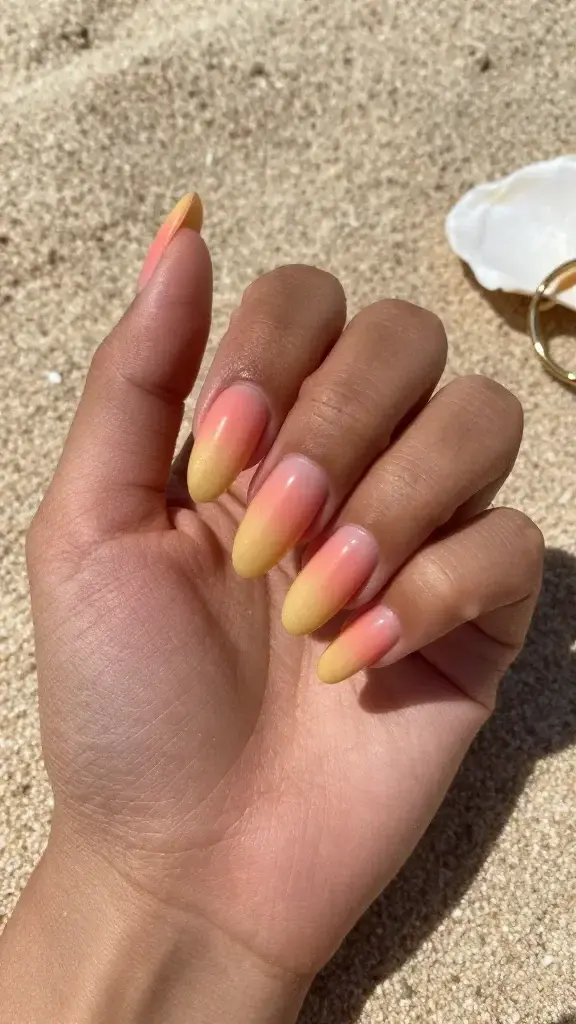 Top-down, hyper-realistic photo of a left hand resting on a sunlit, sandy beach towel, showcasing a fresh “Sunrise Ombré Fade” manicure on medium-length almond nails. Each nail features a smooth gradient: soft coral at the cuticle melting into creamy peach at mid-nail and finishing with golden yellow at the tips, with a seamless blend that suggests a sunrise glow. High-gloss topcoat reflects natural light, emphasizing the lacquer’s shine and smoothness. Subtle micro-shimmer is visible only in the yellow tips for a sunlit effect. Cuticles are clean and moisturized, skin tone is warm-tan with natural texture. Include a soft-focus seashell and a pair of gold hoop earrings partially in frame for summer context. Natural daylight, gentle shadows, realistic color accuracy, no filters, no text, no logos.