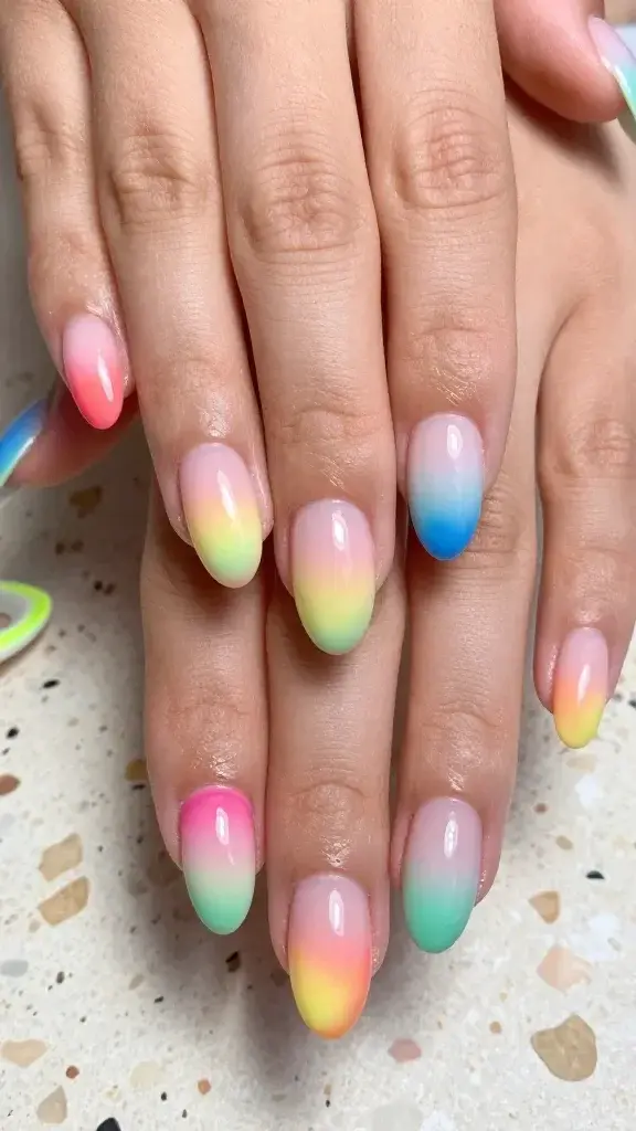 Top-down, hyper-realistic macro photo of a freshly manicured hand with medium-length almond nails showcasing “tropical aura” airbrushed blends. Nails have a sheer milky-pink jelly base with soft, diffused gradients that radiate from the cuticle outward, like sunset clouds. Each nail features a different combo: index hot pink to coral melt (beach Barbie vibe), middle lemon to lime glow (citrus aura), ring turquoise to cobalt fade (ocean blues), pinky hot pink to coral, thumb lemon to lime. The gradients are ultra-soft, hazy, and evenly airbrushed with a subtle luminous sheen, no harsh lines. Natural skin tone, moisturized cuticles, glossy gel topcoat with realistic light reflections. Background is a softly lit, sun-washed terrazzo tabletop with a faint shadow, scattered hints of summer elements out of focus (a neon hair clip and a seashell blur) to enhance seasonal feel. Professional studio lighting, high detail texture of nail surface and skin, 50mm lens look, true-to-life color, no filters, no text.