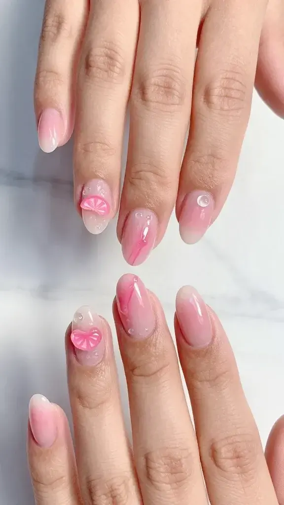 Top-view, hyper-realistic macro photo of two hands with short almond-shaped nails showcasing 3D jelly nail art in a single cool pink color family: translucent blush-to-rose gradient base with a dewy, high-gloss finish; off-center 3D clear gel droplets placed along the outer edge of each nail for a wet effect; subtle, squishy jelly squiggles in slightly deeper pink running diagonally on two accent nails; tiny encapsulated gummy-style charms—one translucent pink heart and one soft pink citrus slice—locked under a domed layer of gel on different nails for depth; no glitter, no harsh reflections, soft daylight from the left, photographed on a pale marble surface with a faint picnic-blanket shadow in the background; skin tone medium with hydrated cuticles, natural hand pose with fingers slightly splayed to showcase texture; editorial beauty photography, ultra-detailed, shallow depth of field, 50mm macro, true-to-life color, no text, no branding.