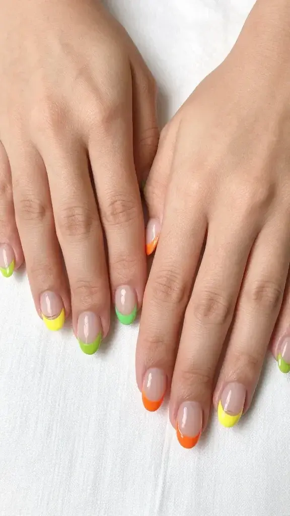 Top-down, hyper-realistic studio photo of both hands resting on a soft white linen surface, showcasing short, neatly filed oval nails with a sheer nude, glossy base and ultra-thin micro-French tips in citrus shades. Each nail features a paper-thin, precise smile line using a nail art pen effect: left hand alternating lemon yellow (thumb, middle), lime green (index, pinky), and tangerine orange (ring); right hand alternating tangerine orange (thumb, middle), lemon yellow (index, pinky), and lime green (ring). The citrus colors are vivid yet elegant with a satin pop against the natural nude base, no visible brushstrokes, edges crisp and symmetrical. Cuticles are clean, moisturized, and natural; skin tone is light-medium with neutral undertones. Lighting is bright, diffused daylight with soft shadows, high-resolution macro clarity showing glossy reflection on each nail. No jewelry, no props, minimalist composition emphasizing the ultra-fine micro-French lines and subtle color mix for a grown-up, playful weekend-brunch vibe.