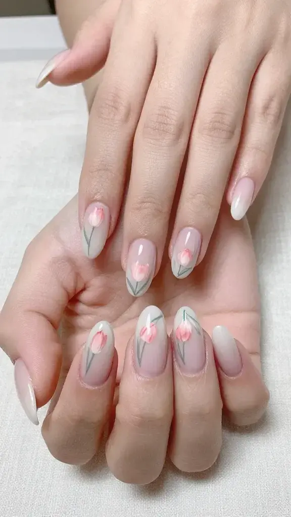 Top-view, high-resolution realistic photo of both hands with medium-length almond nails resting on a soft linen backdrop. Nails feature a sheer milky neutral base with a cloudlike, semi-translucent finish. Along each cuticle line, delicate mini tulip buds are hand-painted: petals in soft blush pink with a whisper of coral at the center for dimension, paired with ultra-fine sage-green stems and subtle curved strokes for natural movement. The tulips vary slightly in size and angle to look organic and graceful, accentuating the almond silhouette. Finish is glossy but not overly reflective. Skin tone is light-medium with natural texture, soft diffused daylight, shallow depth of field focusing on the nail art details. No jewelry, no text, no logos, no extra props—just clean, elegant, romantic floral nail art suitable for a garden party or date night. Photographic realism, beauty editorial quality.