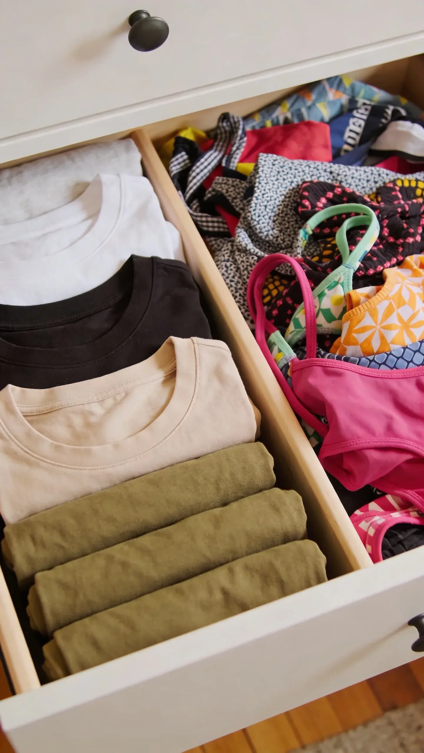 A neatly arranged dresser drawer filled with neutral tees and tanks rolled by color (white, black, beige, olive), next to a drawer of chaotic, bright patterned pieces; overhead view, crisp organization vs visual clutter contrast.