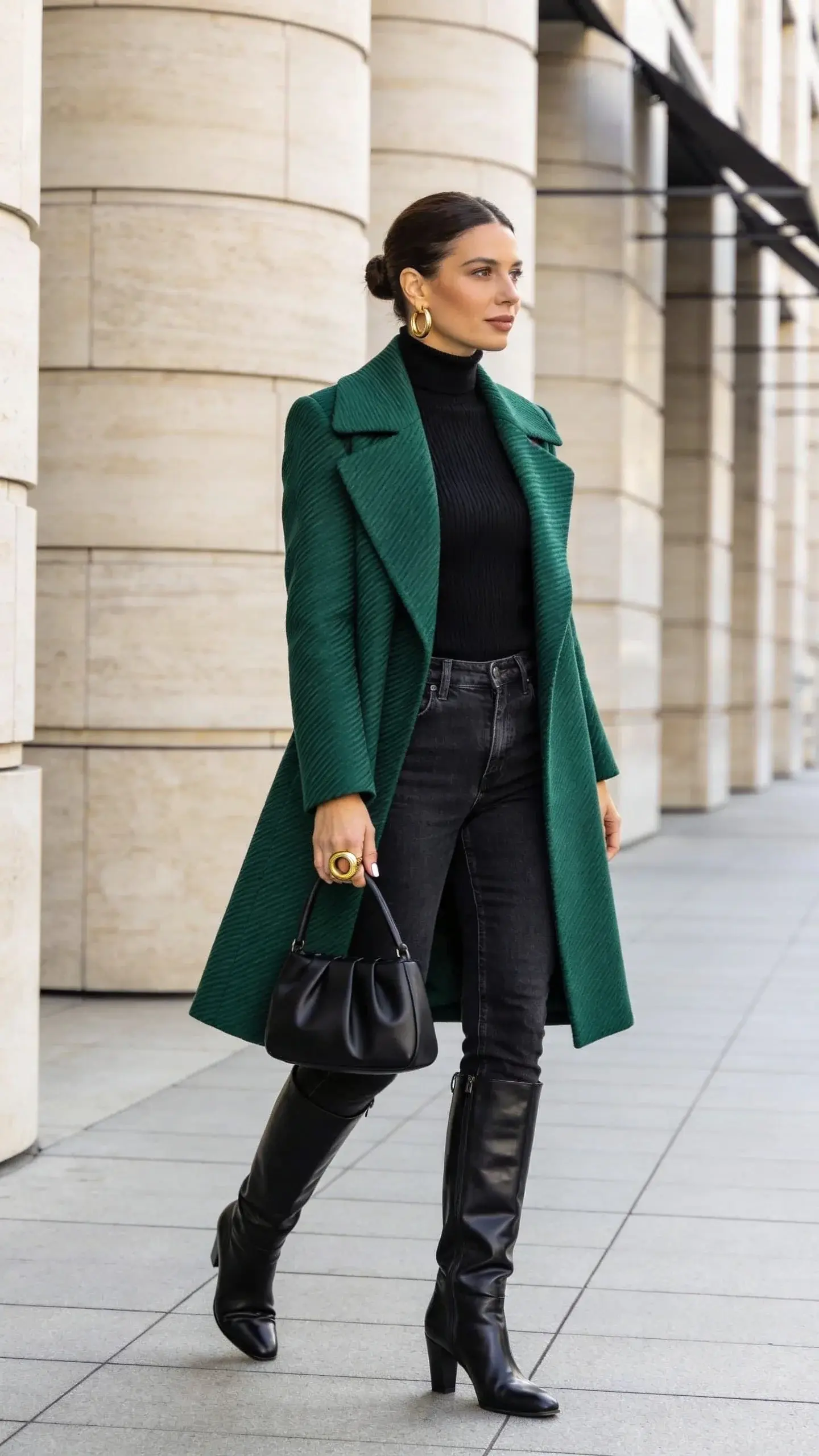 Elegant woman in her late 30s wearing dark-wash straight-leg jeans and a fine merino turtleneck in black, styled with a knee-skimming statement coat in a rich emerald green with subtle herringbone texture; the coat is tailored with strong shoulders and a clean, draped line. She pairs the look with sleek black leather knee-high boots, a structured black top-handle bag, and a single bold gold ring with matching structured gold hoop earrings. The base outfit is fully monochrome black so the coat is the focal point. Natural, polished makeup, glossy low bun, and minimal nails. She stands mid-stride on a clean, modern city sidewalk near limestone architecture and soft morning light, shallow depth of field. Photorealistic fashion street-style photography, full-body, 50mm lens, high dynamic range, crisp textures, no text, editorial yet approachable mood.