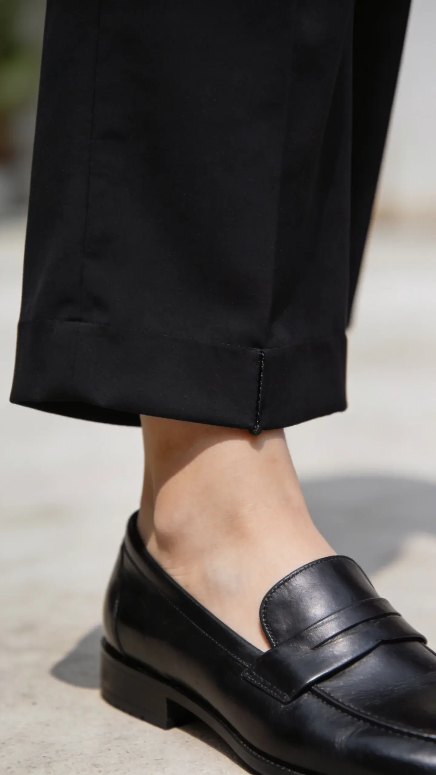 Close-up detail shot of a pair of black wide-leg pants hemmed to hover just above sleek leather loafers; clean break at the ankle, no puddling; rich fabric texture visible, natural daylight, minimal background.