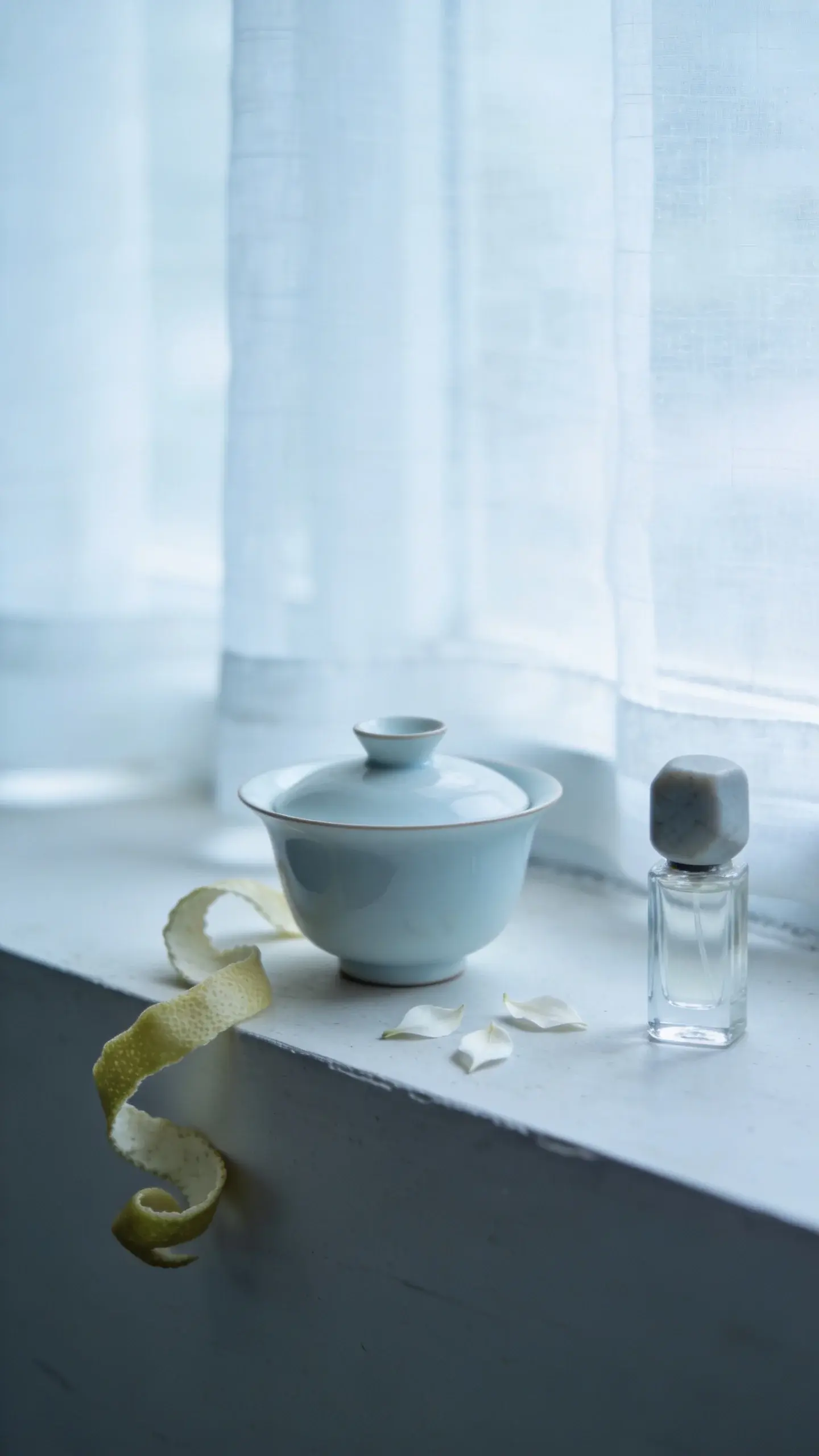 Tea and citrus refinement on a windowsill: a thin porcelain gaiwan, a few scattered white tea leaves, delicate bergamot zest curls, and a small, clear perfume vial with a matte stone cap; cool, overcast daylight filtering through sheer curtains; soft, airy composition; no text.