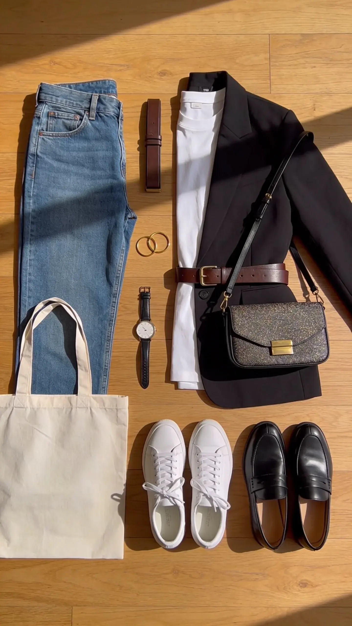 A flat lay on a wooden floor: everyday hero outfit combo for office-to-errands—straight-leg jeans, white tee, black blazer, leather belt, simple gold hoops, watch, white sneakers and black loafers side by side. Add a chic crossbody bag and a reusable tote. Natural shadows, no text.